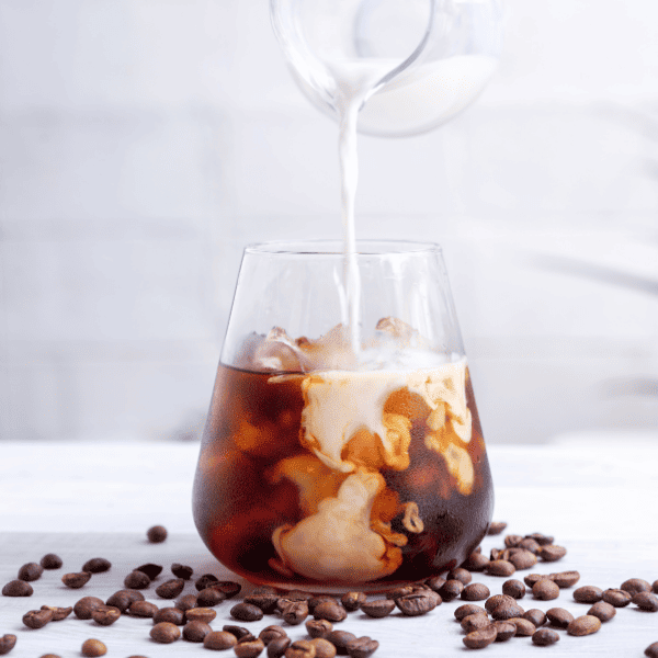 Cold brew coffee with milk on white wooden table.