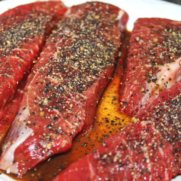 Close-up of raw steaks marinating on a white plate.