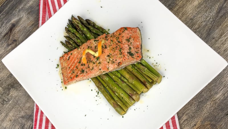 honey orange glazed salmon served over asparagus on a while plate