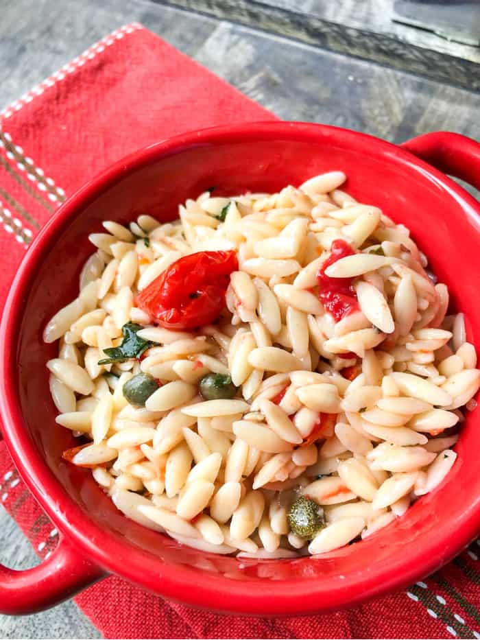 vertical image of the vegan orzo pasta salad in a red bowl