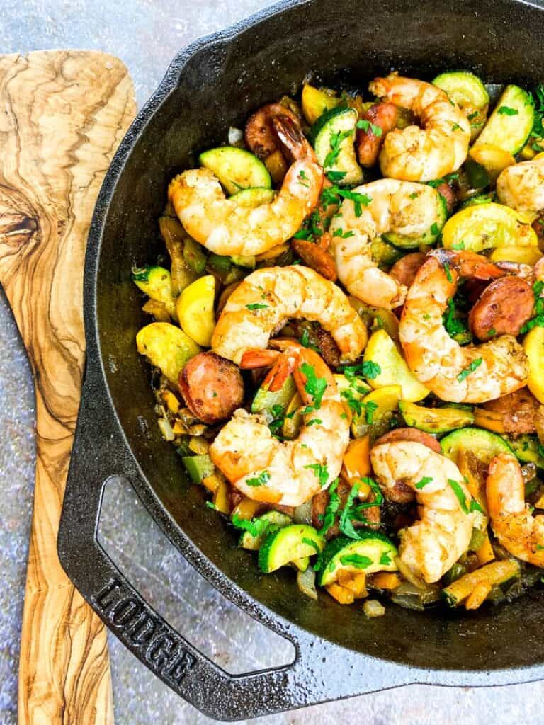 cooked shrimp and vegetable dish in a cast iron pan with a wooden spoon