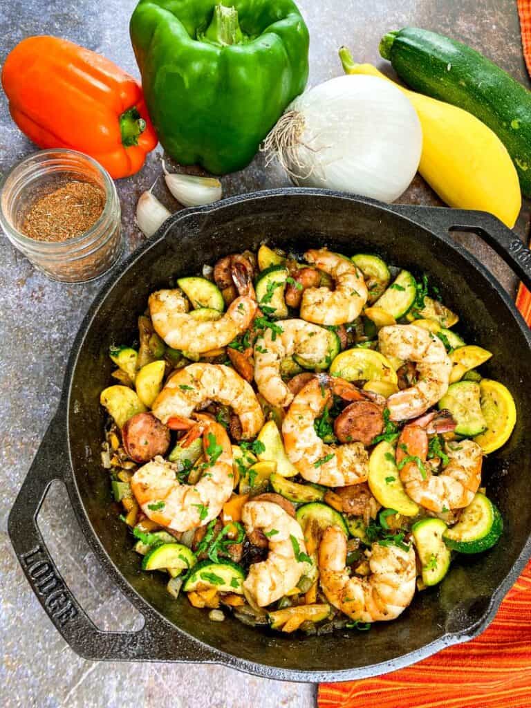Easy Cajun Shrimp and Vegetable Skillet Meal in a cast iron pan surrounded by veggies