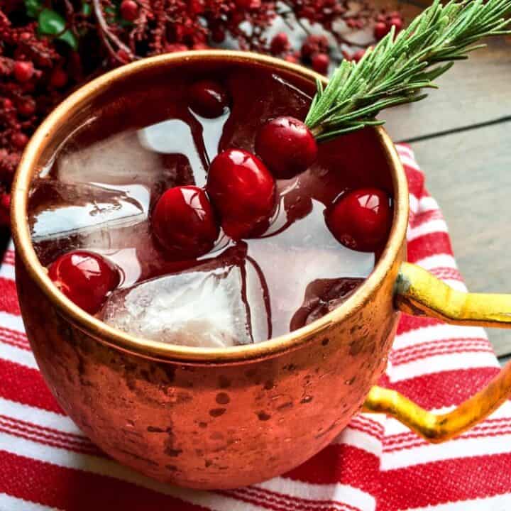 cranberry mule in a copper cup garnished with fresh cranberries on a rosemary sprig