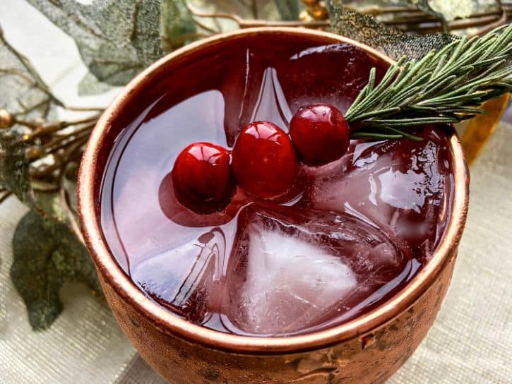 cranberry cocktail mule in copper cup with sprig of rosemary and fresh cranberries
