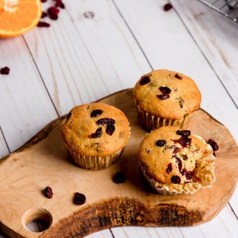 orange cranberry muffins on wood slice cutting board