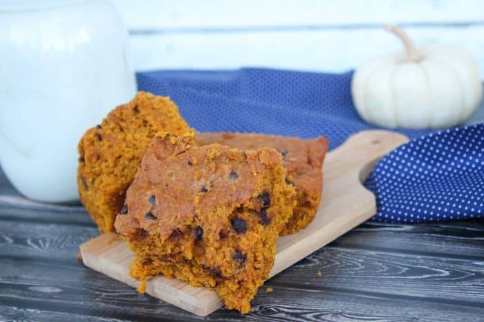 chewy pumpkin blondies on a cutting board with glass of milk and white pumpkin in background