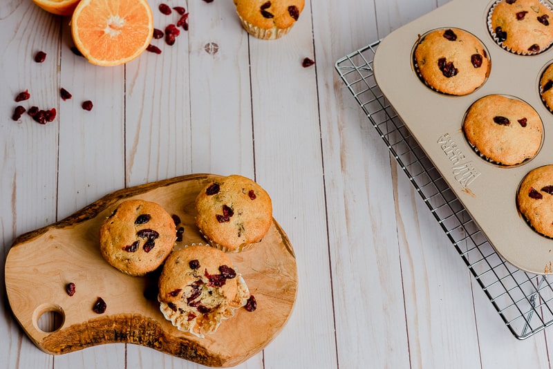vegan orange cranberry muffins on white wood background with orange slices and cranberries