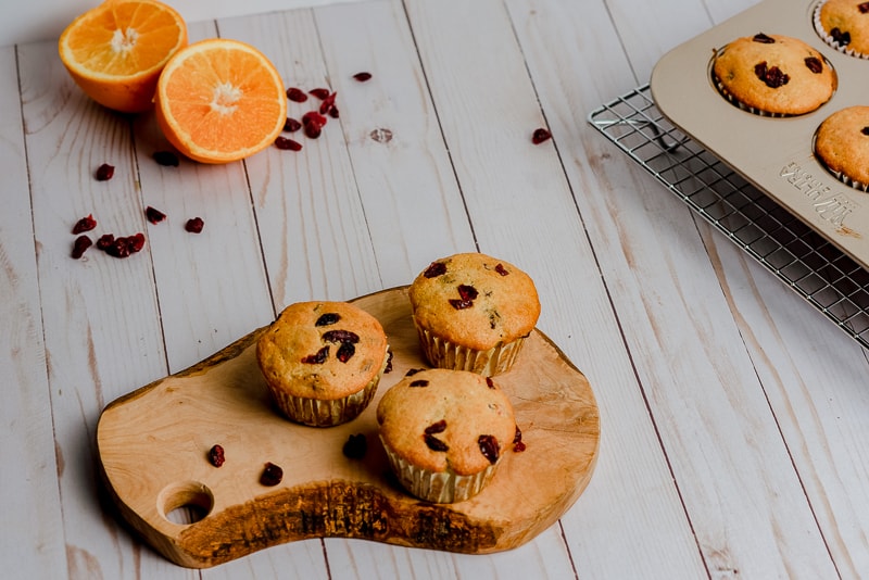 three cranberry muffins on wood slice