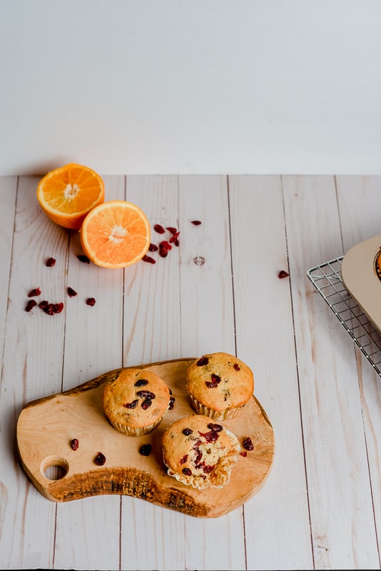 vegan cranberry orange muffins on white background with wood slice cutting board