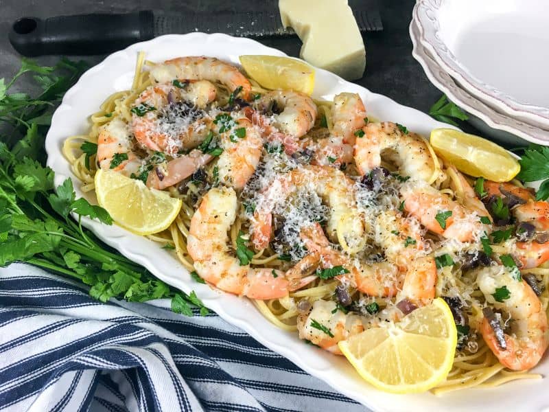 shrimp scampi over spaghetti garnished with lemon wedges and parmesan cheese