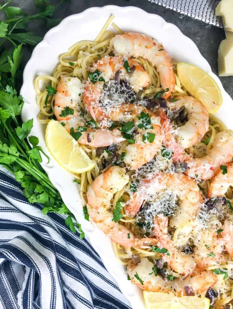 delicious shrimp scampi with spaghetti on a white platter garnished with lemon wedges