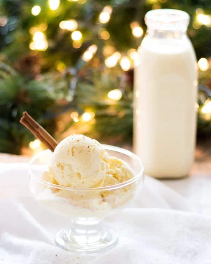 eggnog ice cream in glass bowl with eggnog and tree in background