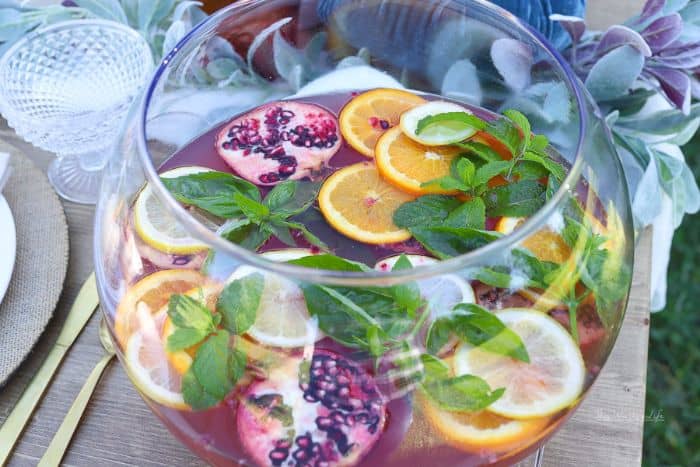 citrus soda punch in large clear punch bowl garnished with orange slices, pomegranate and mint leaves