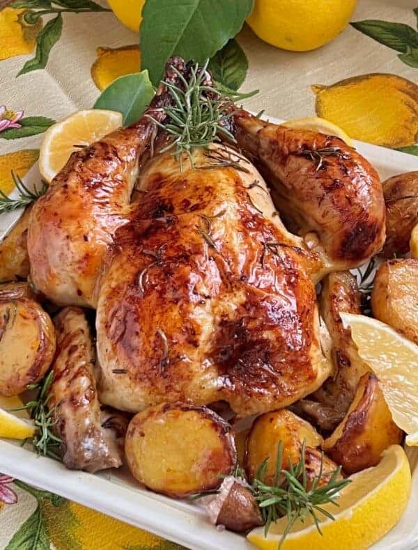 rosemary citrus roast chicken in white plate surrounded by potatoes and lemons