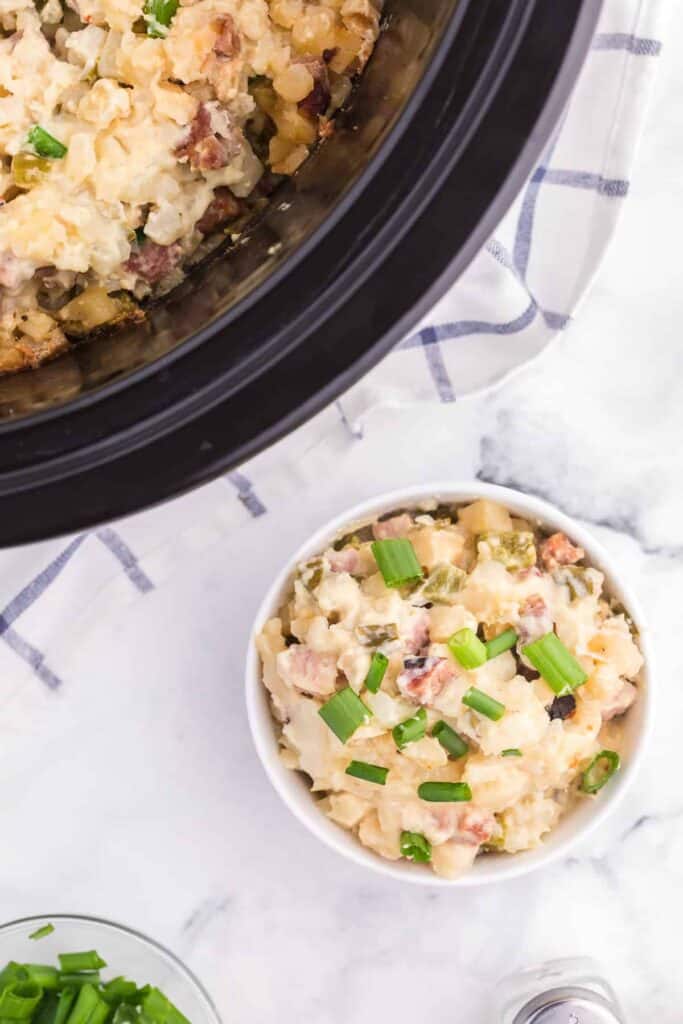 slow cooker ham and potato hash in white dish with view of crock pot