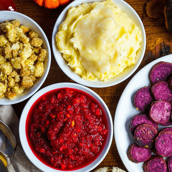 Side vegetables plated and on table, mashed potatoes, cranberries, stuffing and purple potatoes.