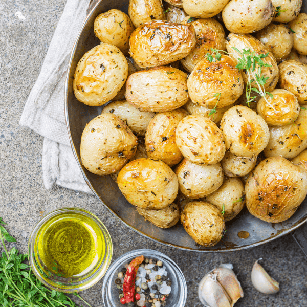 Roasted baby potatoes with greens and garlic oil over stone background.