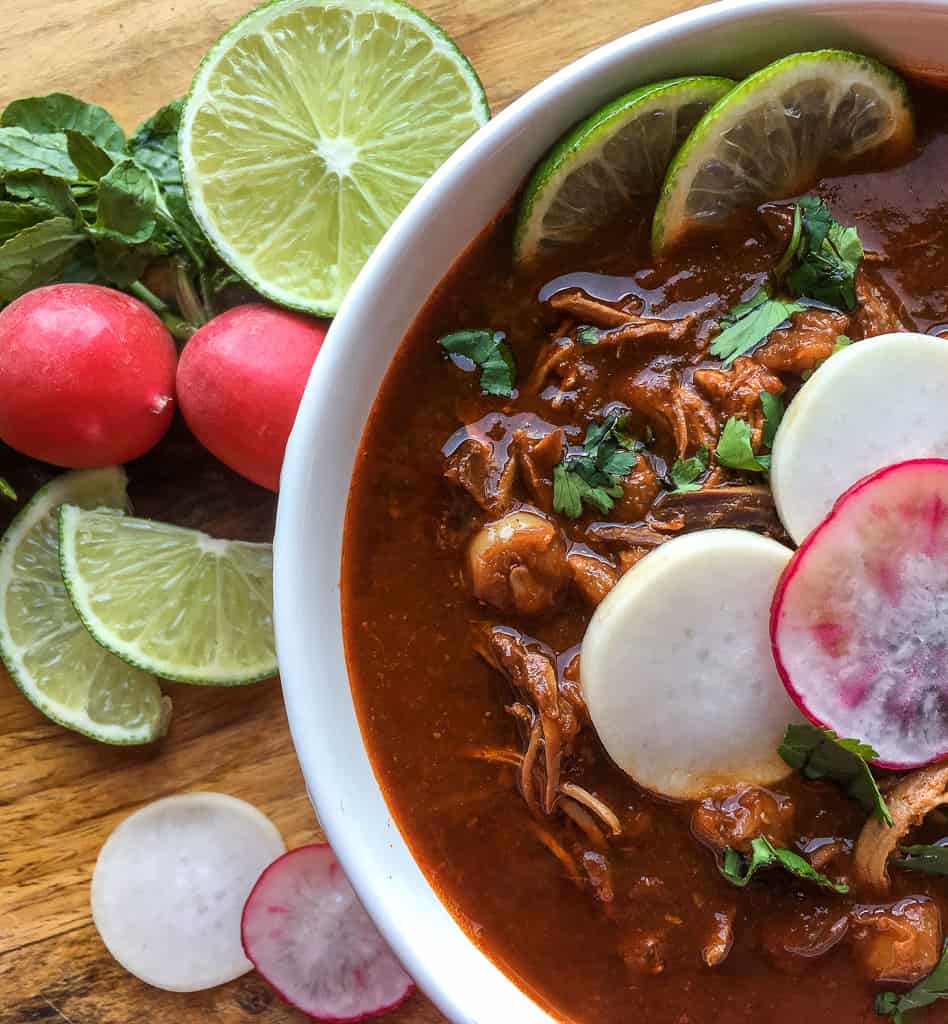 Pozole Rojo de Pollo served on white bowl and wood background.