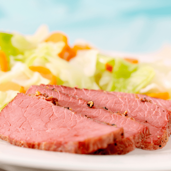 Corned beef and cabbage served on a white plate on a blue background.