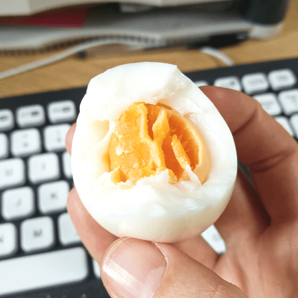 A hand holding a half eaten hard boiled egg.