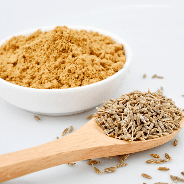 Cumin in soup: Powder cumin in a small white bowl and a wooden spoon filled with cumin seeds on white background.