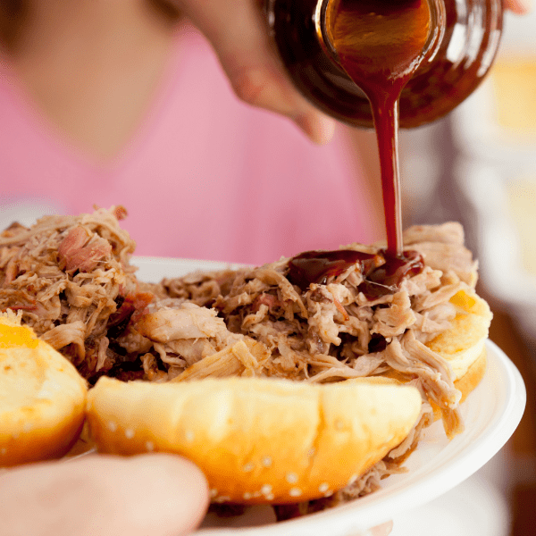 Pouring BBQ sauce to a pulled pork sandwich.
