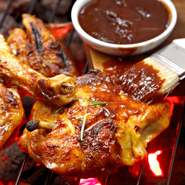 Grilled chicken next to a bbq brush and bbq sauce