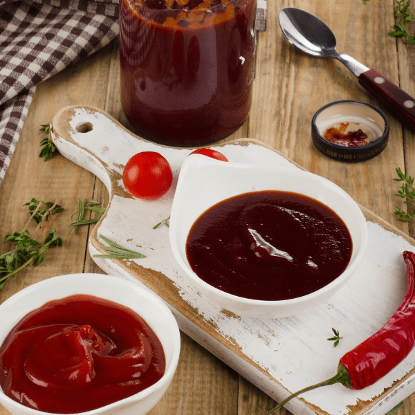 A bowl of tomato and a a bowl of BBQ Sauce