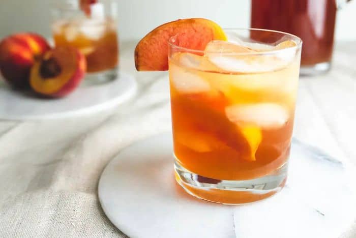 bourbon peach tea in small glass with peach garnish