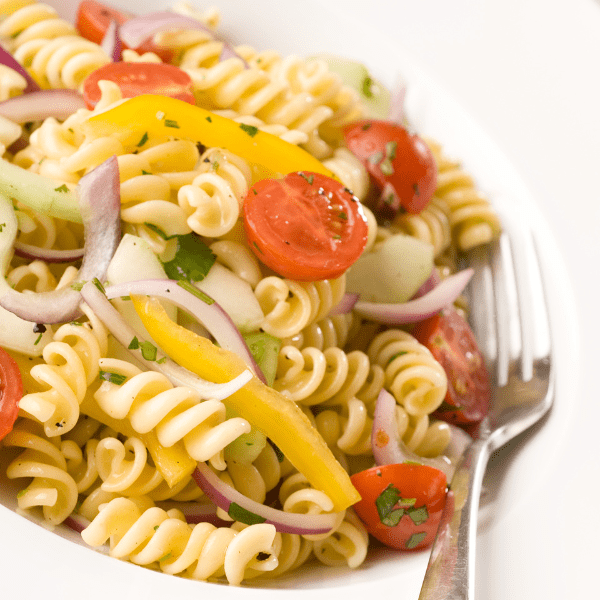 Close up of pasta salad served in a white dish with a fork next to it.