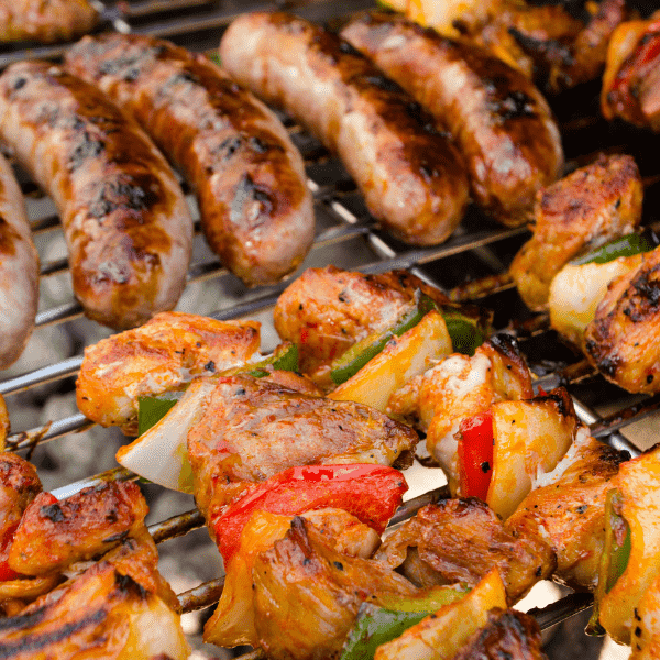 Close up of sausages and chicken kabots cooking in the grill.