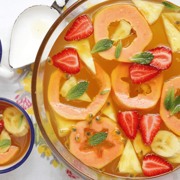 Colorful fruit punch with fresh strawberries, pineapple, banana and mint served on a table.