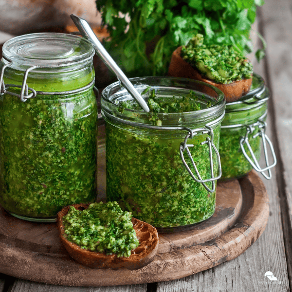 Glass jars of pesto and slices of toast with pesto spread.