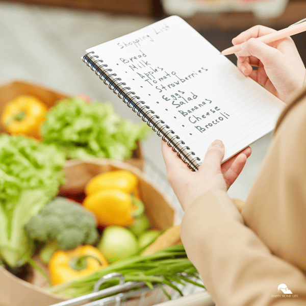 An image of a hand holding a shopping list. Different fruits and vegetables are seen in the background.