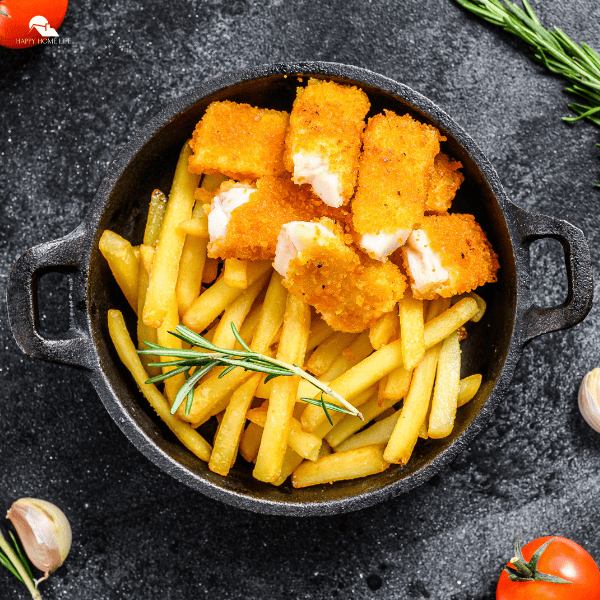 An image of fried fish and fries in a cast iron pan. Parts of vegetables and herbs are also seen in the borders of the image.