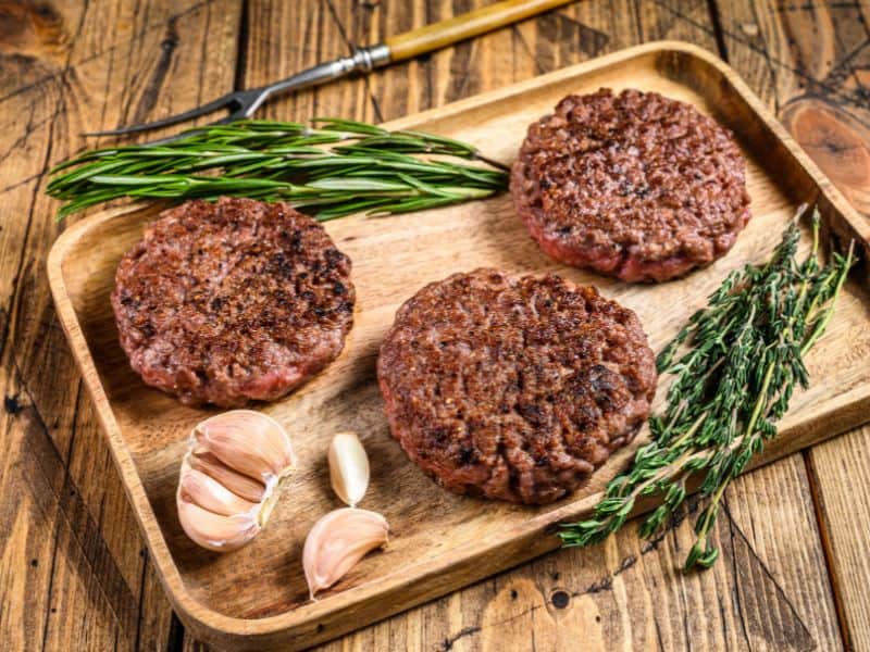 three cooked hamburger patties on wooden tray