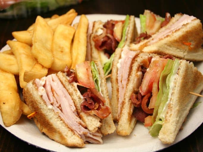 turkey club sandwich divided in quarters served with fries