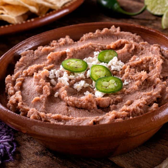 brown bowl of refried beans topped with jalapeno slices