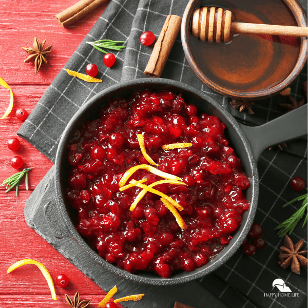 An image of cranberry sauce, with a bowl of honey on the side, and scattered cranberries, fresh thyme, cinnamon bark and star anise.