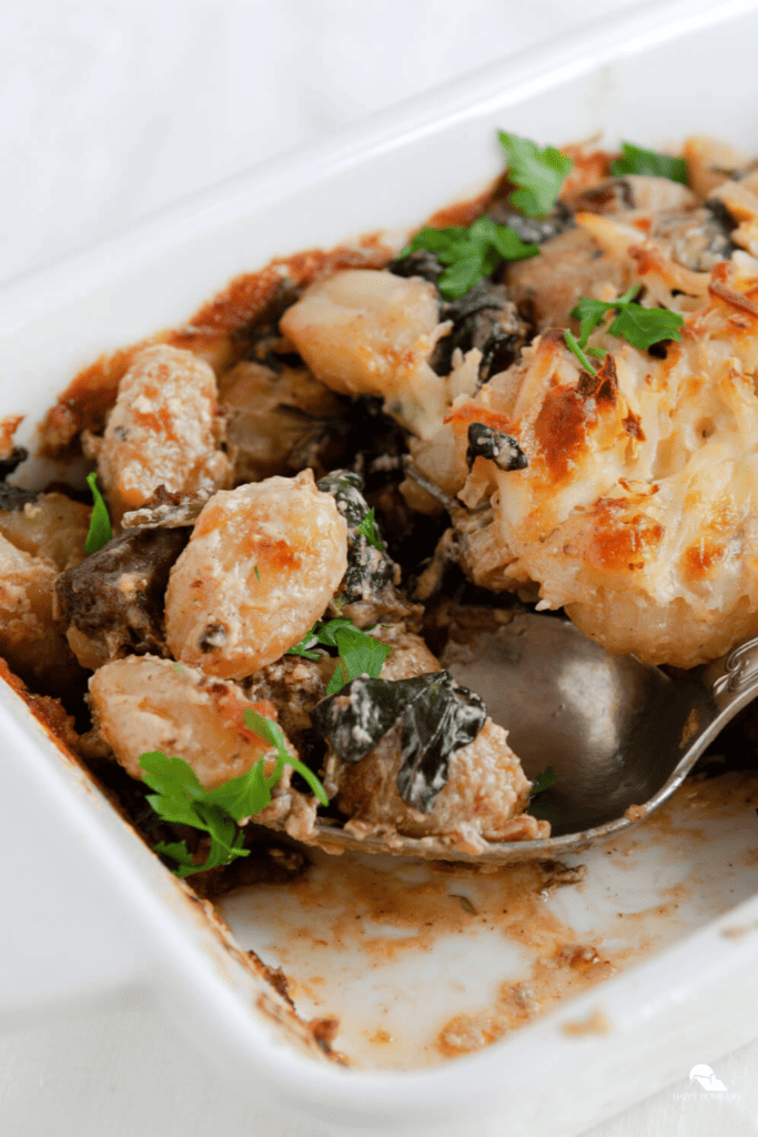 a vertical image of Baked Gnocchi in a white plate with a spoon used to scoop