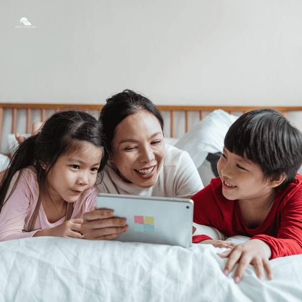 Cheerful mother watching video via tablet with kids on bed