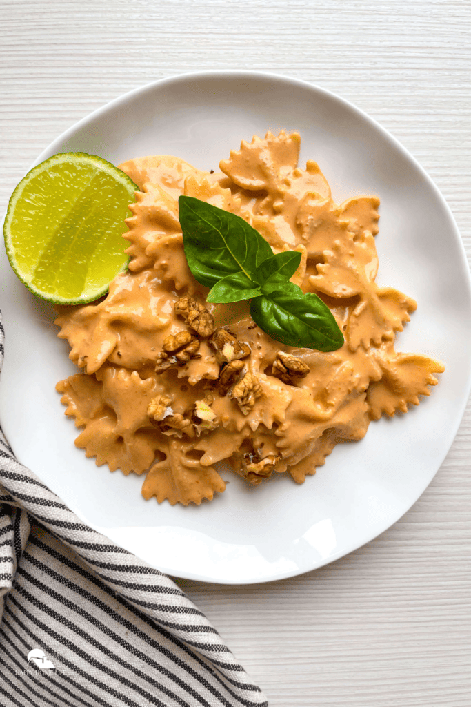 Pasta with Roasted Red Pepper Walnut Sauce in a white plate with cloth beside it