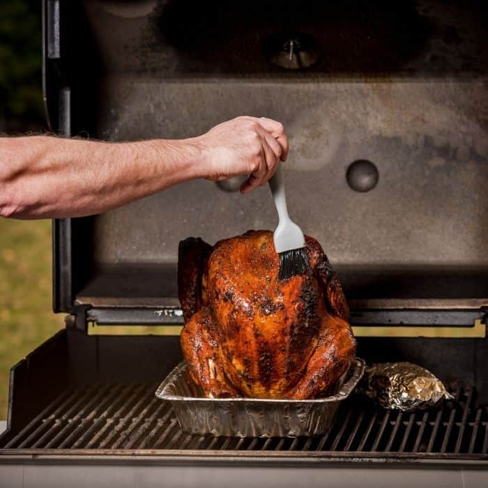 man basting turkey on a grill
