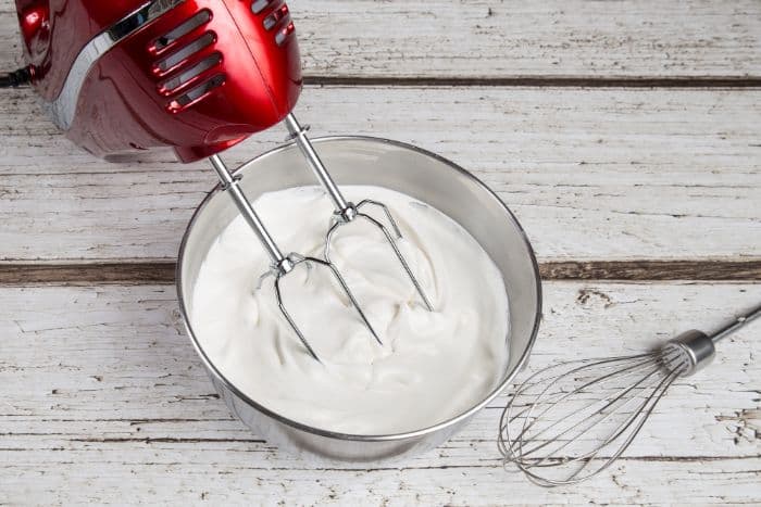 red mixer with beaters in bowl of freshly whipped cream