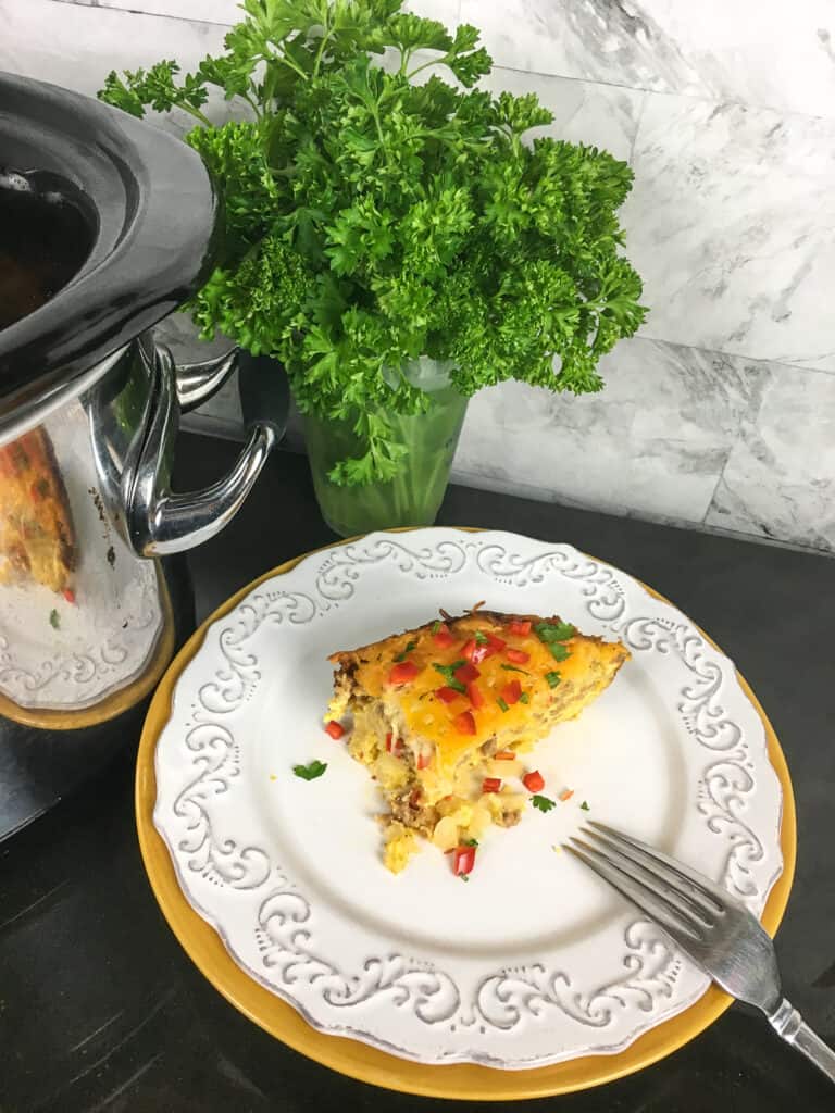 Slice of Southwestern breakfast casserole on a plate with fork and parsley in the side. 