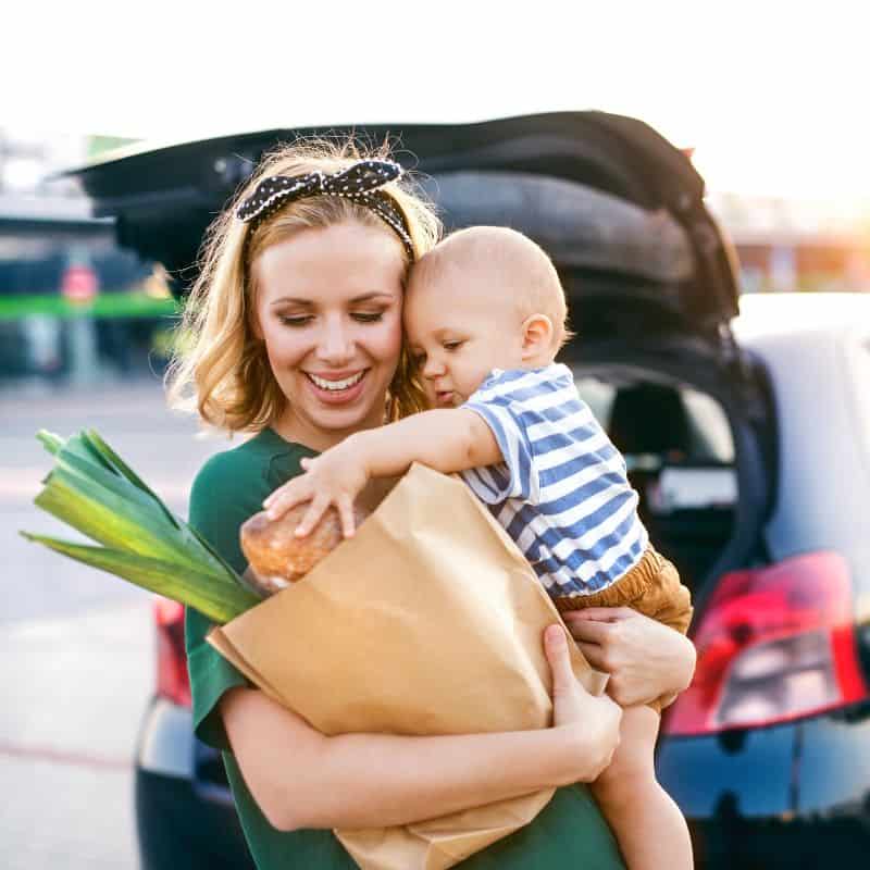mom with baby and groceries in front of car with open trunk