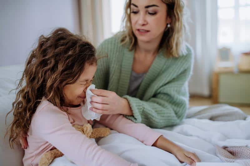 girl blowing her nose while mom holds tissue