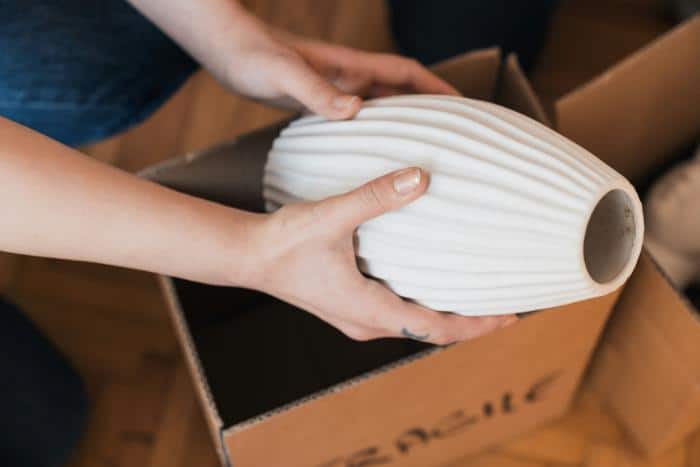 hands packing a piece of decor (like a vase) into a box marked "fragile"