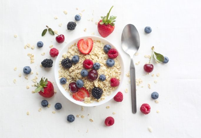 oatmeal in white bowl topped with berries with spoon off to the right and additional berries around the bowl