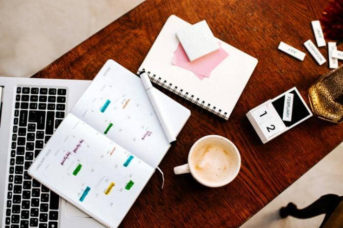 planner, laptop, notebooks, and coffee on wooden table